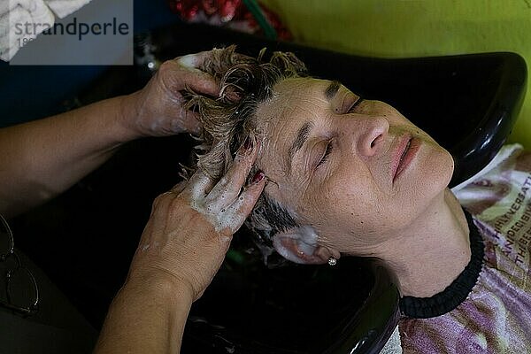 Nahaufnahme einer reifen Kundin  die sich von einem Friseur die Haare waschen lässt  nachdem sie sich im Schönheitssalon die Haare gefärbt hat. Kleine lateinische Schönheitssalon Geschäft