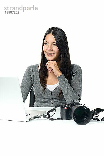Attraktive Fotografin  die sich in ihrem Stuhl zurücklehnt und zufrieden über ihre Aufnahmen lächelt  während sie auf den Bildschirm ihres Laptops mit der Kamera in der Nähe schaut