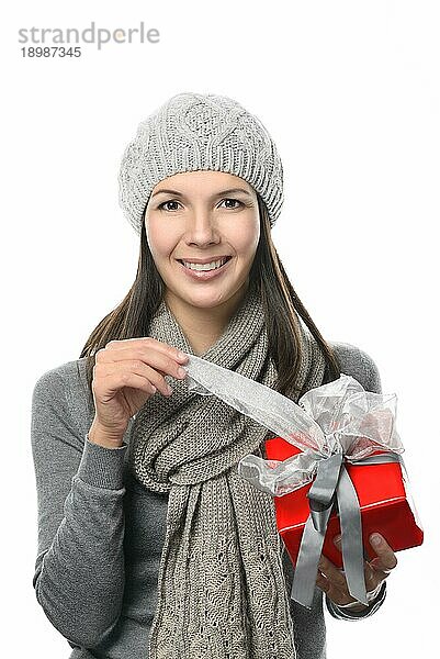 Close up Hübsche lächelnde junge Frau in Wintermode hält Geschenkbox während Blick auf Kamera  vor weißem Hintergrund