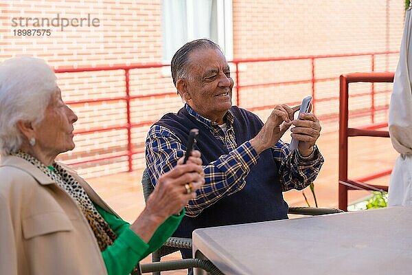 Zwei ältere Menschen im Garten eines Pflegeheims  die auf das Telefon schauen  Technologien im Alter