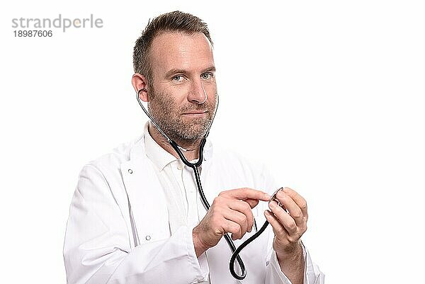 Lächelnder  unrasierter  männlicher Arzt  der ein Stethoskop in der Hand hält und bereit ist  eine Untersuchung durchzuführen  während er in die Kamera blickt  vor weißem Hintergrund