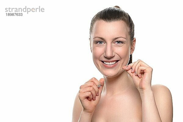 Lächelnde attraktive nackte Frau mit einem zahnigen Lächeln  die Zahnseide zwischen ihren Händen hält  in einem Konzept für Zahnpflege und Mundhygiene  vor weißem Hintergrund