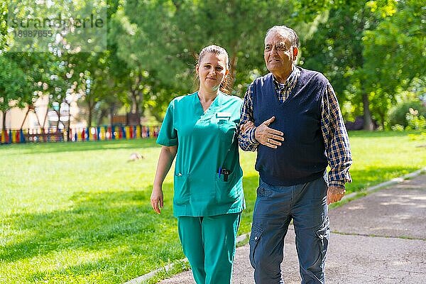 Ein älterer Mann mit der Krankenschwester bei einem Spaziergang durch den Garten eines Pflegeheims