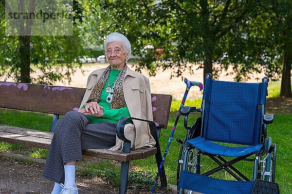 Porträt einer älteren Frau  die auf einem Stuhl im Garten eines Pflegeheims im Rollstuhl sitzt