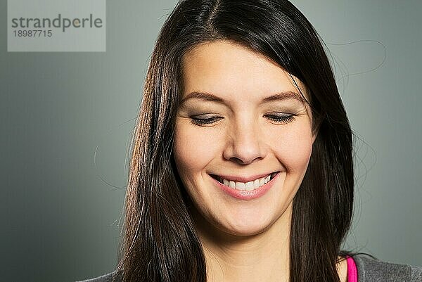 Glückliche  zufriedene Frau mit einem strahlenden Lächeln und geschlossenen Augen  Gesichtsporträt in Nahaufnahme auf grauem Studiohintergrund