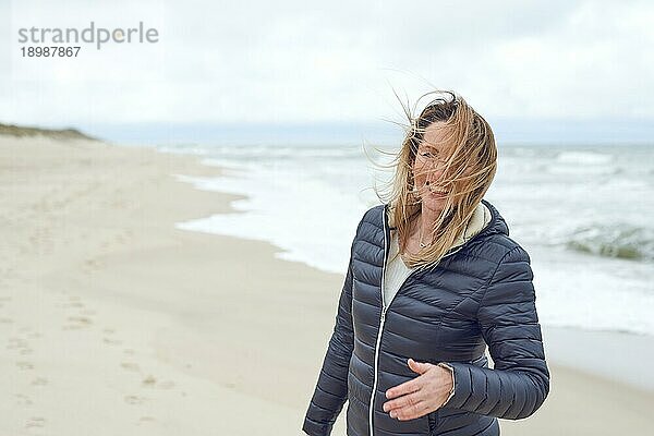 Lächelnde Frau an einem windigen  menschenleeren Strand  die lacht  während der Wind ihr Haar über ihr Gesicht weht  mit Kopiervorlage