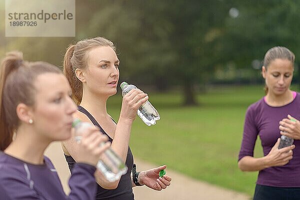 Sportliche Frauen trinken Wasser  während sie sich nach einem Outdoor Training im Park ausruhen