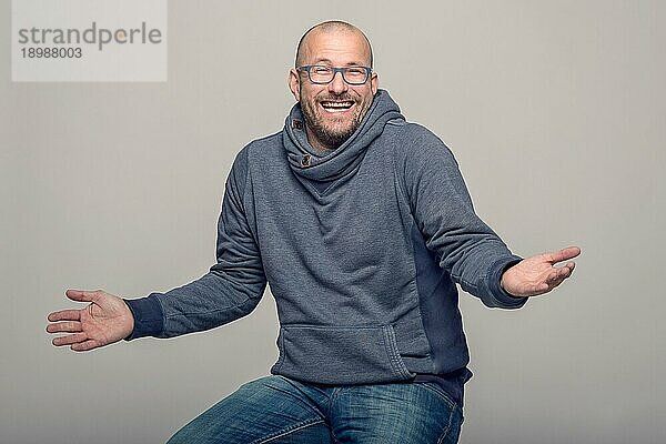 Charismatischer  glatzköpfiger Mann mittleren Alters mit Brille  der lachend mit den Schultern zuckt  um seine Unwissenheit zu zeigen  sitzender Oberkörper über grauem