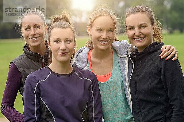 Vier glückliche  gesunde  junge Frauen in einer Reihe  die sich nach ihrer Outdoor Übung umarmen und in die Kamera lächeln