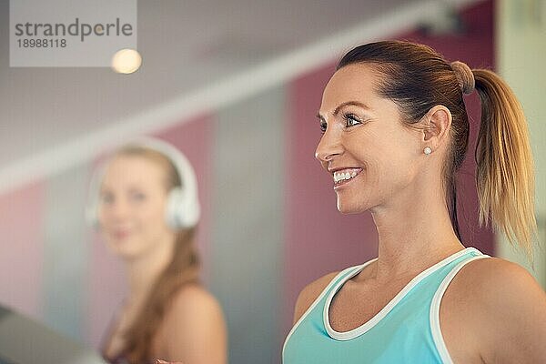 Attraktive Frau mittleren Alters in einem mintfarbenen Top steht auf dem Laufband im Fitnessstudio  schaut in die Kamera und lächelt mit Kopie Raum