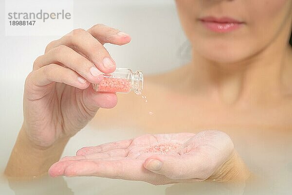 Frau  die ein verjüngendes therapeutisches Aromatherapie Bad in einem Spa genießt und in das warme Seifenwasser eintaucht  während sie mit einem glücklichen Lächeln der Vorfreude Badesalzkristalle in ihre Hand gießt