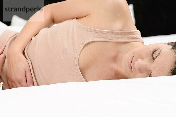 Frau mit monatlichen Menstruationsschmerzen  die ihren Bauch mit den Händen umklammert  während sie durch die anhaltenden Krämpfe gestresst wird  während sie in ihrem Bett sitzt
