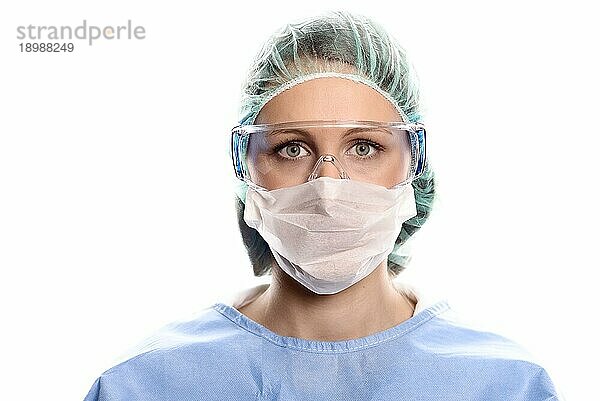 Junge Krankenschwester oder Ärztin in OP Kleidung mit OP Kittel  Maske  Schutzbrille und Kappe  die direkt in die Kamera blickt  Kopf und Schultern vor weißem Hintergrund