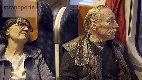 Ein älteres Ehepaar reist im Zug  der Senior schaut aus dem Fenster  eine Frau schläft