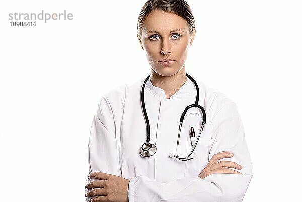 Seriöse selbstbewusste Ärztin oder Krankenschwester mit Brille  stehend mit verschränkten Armen in einem weißen Laborkittel  mit einem Stethoskop um den Hals  vor weißem Hintergrunder selbstbewusste Ärztin oder Krankenschwester mit Brille  mit