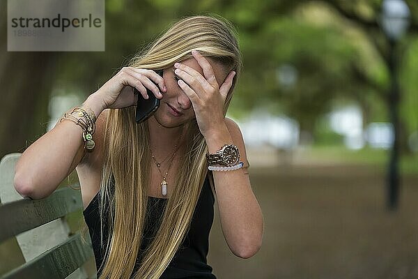 Ein blondes Teenagermodell spricht in einer Umgebung im Freien mit einem Mobiltelefon