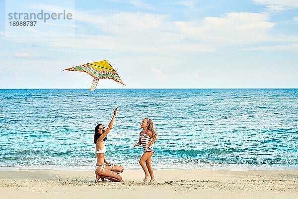 Mutter und Tochter haben Spaß beim Fliegen eines Drachens am tropischen Strand. Familienurlaub  Strand Spaß Konzept