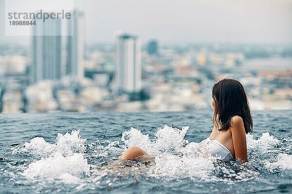 Junge Frau entspannt sich im Jacuzzi auf dem Dach des Hotels und genießt die Aussicht auf die Stadt. Sommerurlaub Konzept