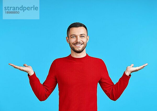 Gutaussehender glücklicher Mann  der Copy Space vorblauem Hintergrund präsentiert. Präsentiert Produkt und Werbekonzept