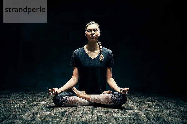Junge attraktive Frau übt Yoga sitzen in Lotuspose und meditieren in dunklen Raum. Ardha Padmasana Übung. Gleichgewicht und Erholung Konzept