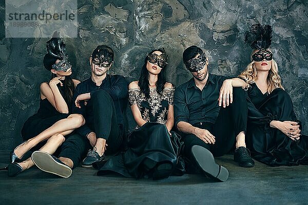 Gruppe von Freunden in Maskerade Karneval Maske sitzen auf dem Boden entspannen nach der Party. Schöne Frauen und Männer tragen venezianische Maske. Mode  Freunde Konzept