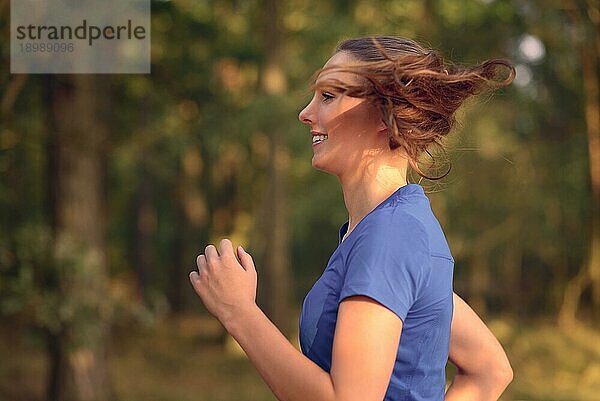 Nahaufnahme einer fröhlich lächelnden jungen Frau  die in der Natur joggt  während sie ihre täglichen Übungen in einem Gesundheits und Fitnesskonzept absolviert