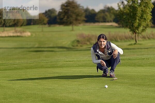 Eine Golferin  die einen Putt ausführt  kniet auf dem Grün und schaut auf das Loch  um das Gras und die eventuelle Wölbung eines Hangs zu prüfen