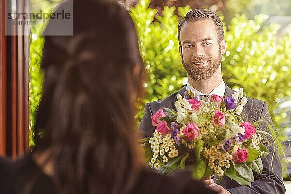 Handsome Bearded Guy Giving einen Strauß frischer Blumen zu seiner Freundin mit glücklichen Gesichtsausdruck