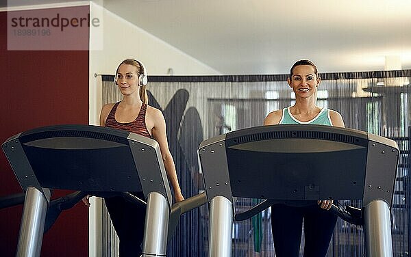 Attraktive junge Frau mit drahtlosen Kopfhörern steht auf dem Laufband im Fitnessstudio  schaut in die Kamera und lächelt mit Kopie Raum