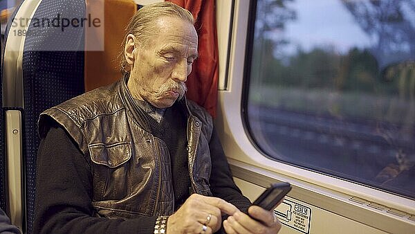 Senior mit Brille reist in einem Zug und benutzt morgens ein Smartphone