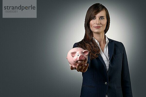 Lächelnde erfolgreiche Geschäftsfrau  die ein Sparschwein in den Händen hält  das Reichtum  Ersparnisse  Investitionen und Sicherheit symbolisiert  in Grau mit Leerzeichen