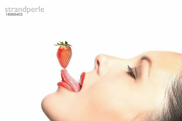 Seitenansicht einer schönen Frau  die eine Erdbeere auf ihrer Zungenspitze balanciert