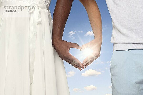 Young Couple Crossing ihre Arme und bilden ein Herz geformte Hände zusammen gegen sonnigen blaün Himmel