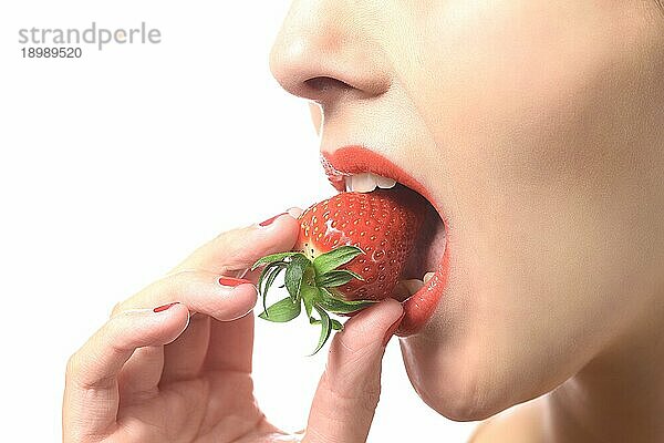 Schöne Frau mit sinnlichen roten Lippen ißt eine üppige reife rote frische Erdbeere mit ihren Lippen in Erwartung des Leckerbissen gescheitelt  Nahaufnahme Teilansicht ihres Gesichts vor weißem Hintergrund