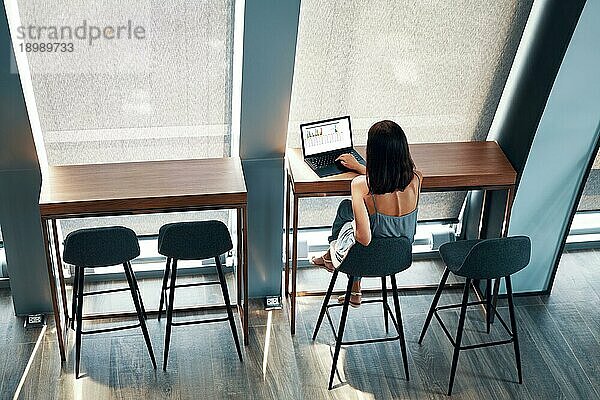 Draufsicht auf eine junge schöne Frau  die an einem Laptop in einem modernen Büro oder Café arbeitet