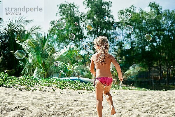 Rückansicht eines kleinen glücklichen Mädchens  das Seifenblasen am aktuellen Strand spielt. Kindheit  LifestyleKonzept