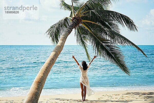 Rückansicht einer glücklichen jungen Frau  die ihren tropischen Strandurlaub unter einer Palme genießt. Sommer Konzept