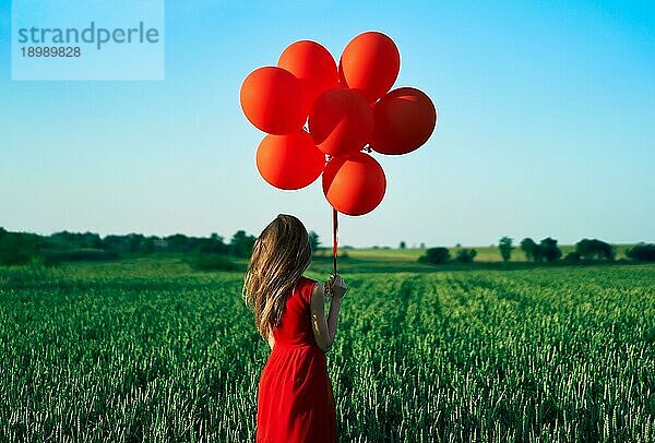 Rückenansicht der Freiheit glückliche Frau läuft mit roten Luftballons auf grünen Sommerfeld. Spaß  Glück Konzept