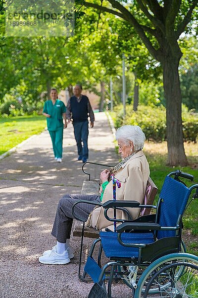 Porträt einer älteren Frau  die auf einem Stuhl im Garten eines Pflegeheims im Rollstuhl sitzt