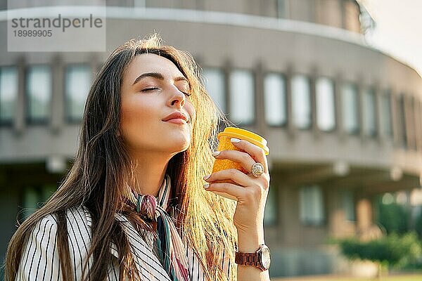 Junge stilvolle Frau auf der Straße trinkt Morgenkaffee im Sonnenlicht. Pause Zeit Konzept