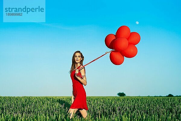 Freiheit glückliche Frau läuft mit roten Luftballons auf grünem Sommerfeld. Spaß  Glück Konzept
