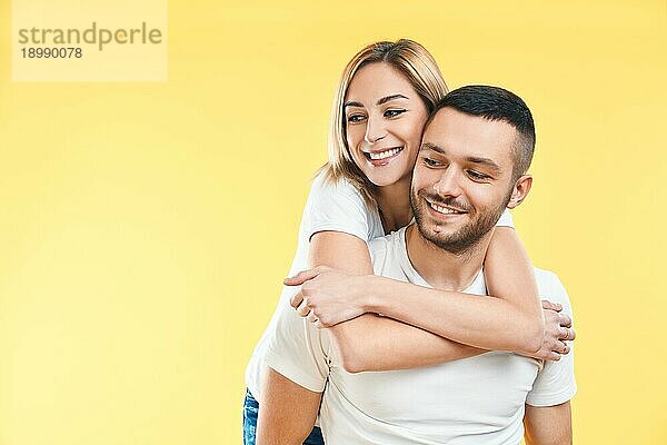 Glückliches  lächelndes  verliebtes Paar auf gelbem Hintergrund mit Kopierraum. Mann trägt seine Freundin Huckepack. Liebe  Romantik  Spaß Konzept