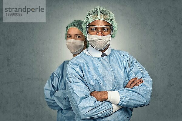 selbstbewusste männliche und weibliche medizinische Fachkräfte  die in die Kamera lächeln und blaue Kittel und Sterilitätskappen tragen