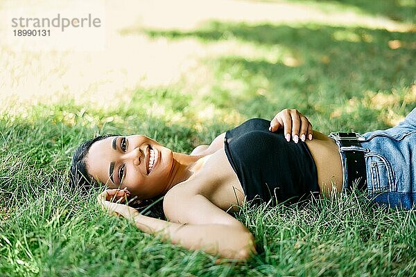 Porträt der hübschen glücklichen afroamerikanischen Frau  die sich auf dem Gras im Park entspannt. Ruhe  weibliche Schönheit Konzept