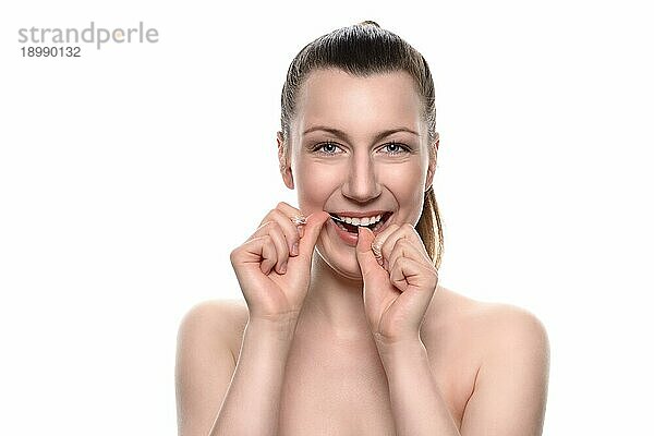 Lächelnde attraktive nackte Frau mit einem zahnigen Lächeln  die Zahnseide zwischen ihren Händen benutzt  in einem Konzept für Zahnpflege und Mundhygiene  vor weißem Hintergrund
