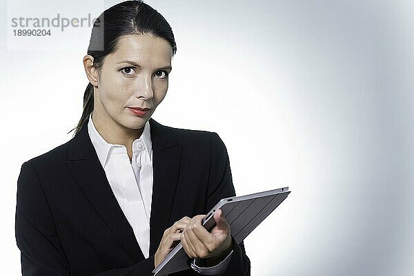 selbstbewusste Business Managerin  die an einem Tabletcomputer arbeitet  während sie mit ernstem  nachdenklichem Gesichtsausdruck in die Kamera schaut  Studioporträt mit Kopierbereich