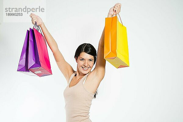 Brünette glückliche junge Frau mit erhobenen Armen  die Einkaufstaschen aus Papier halten  auf grauem Hintergrund