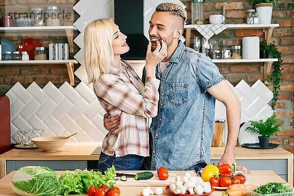 Schönes junges Paar füttert sich gegenseitig und lächelt beim Kochen in der Küche zu Hause. vegetarisch  Beziehung Konzept