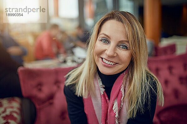 Attraktive Frau mittleren Alters  die in einem Restaurant sitzt und in die Kamera lächelt