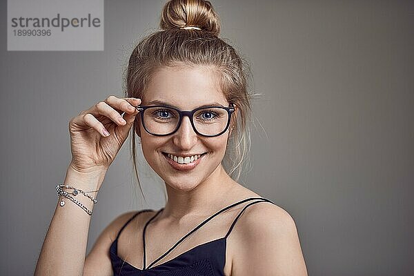 Attraktive  stilvolle blonde Frau mit einem Dutt und einer Brille  die in die Kamera lächelt